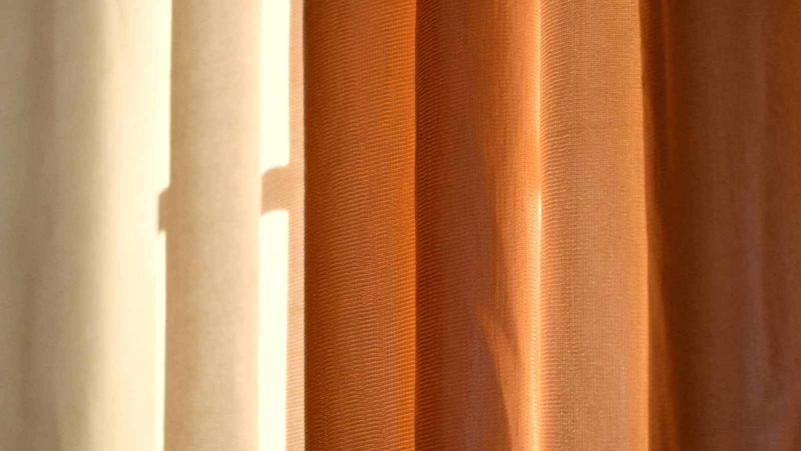Warm sunlight filtering through layered terracotta and cream sheer curtains.